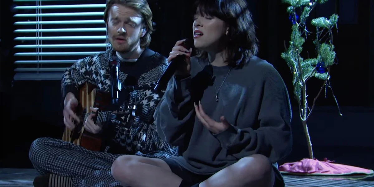 Billie Eilish and Finneas performing in a dimly lit intimate setting with cinematic atmosphere