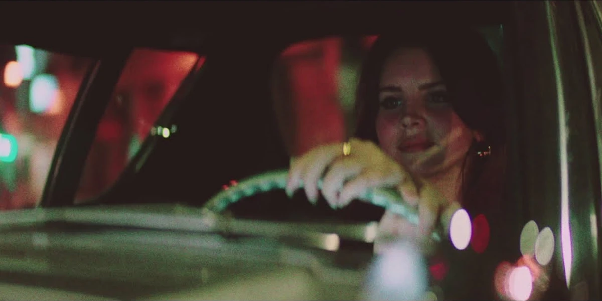 Lana Del Rey driving at night with blurred city lights surrounding the car