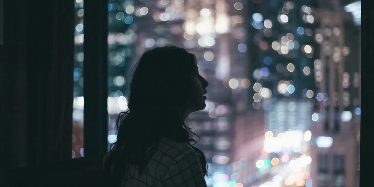 Person sitting alone near a window at night surrounded by blurred city lights