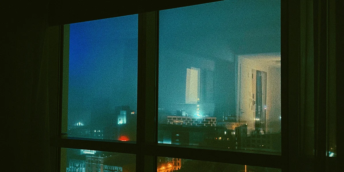 Night city lights viewed through a dark apartment window during a quiet late night atmosphere