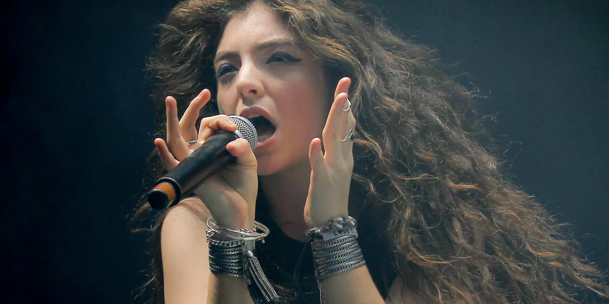 Lorde singing live on stage with an emotional expression and dramatic lighting